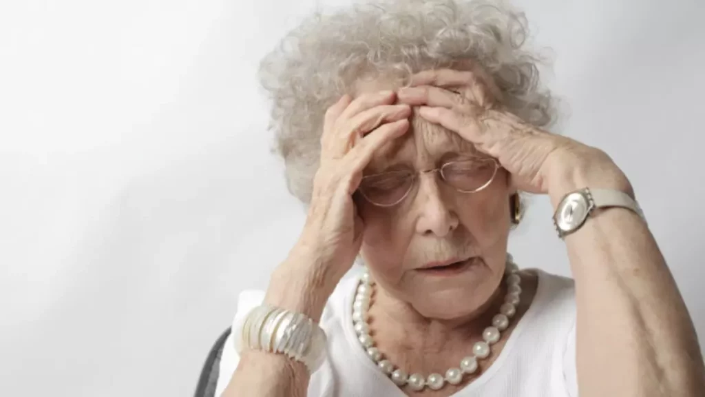 idosa com as duas mãos na cabeça de olhos fechados e cabeça baixa