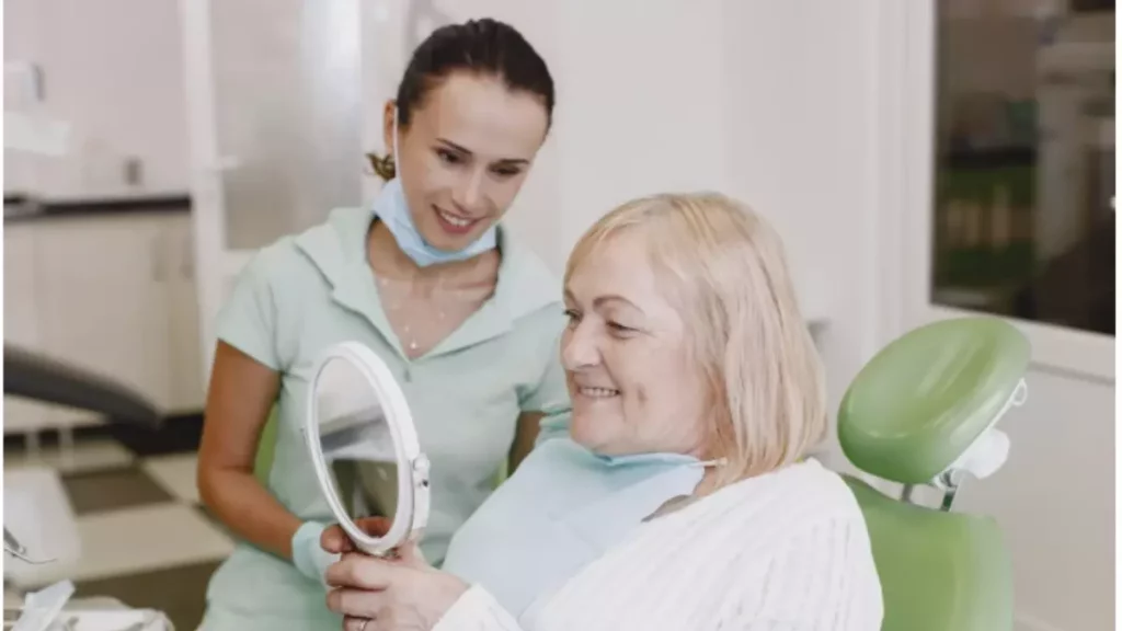 senhora se olhando no espelho e apreciando seu sorriso ao lado de sua dentista